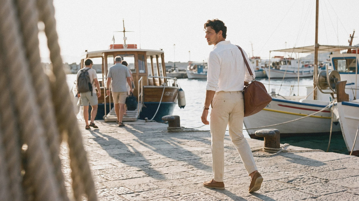 Man carrying a brown leather weekend bag along a harbour quay