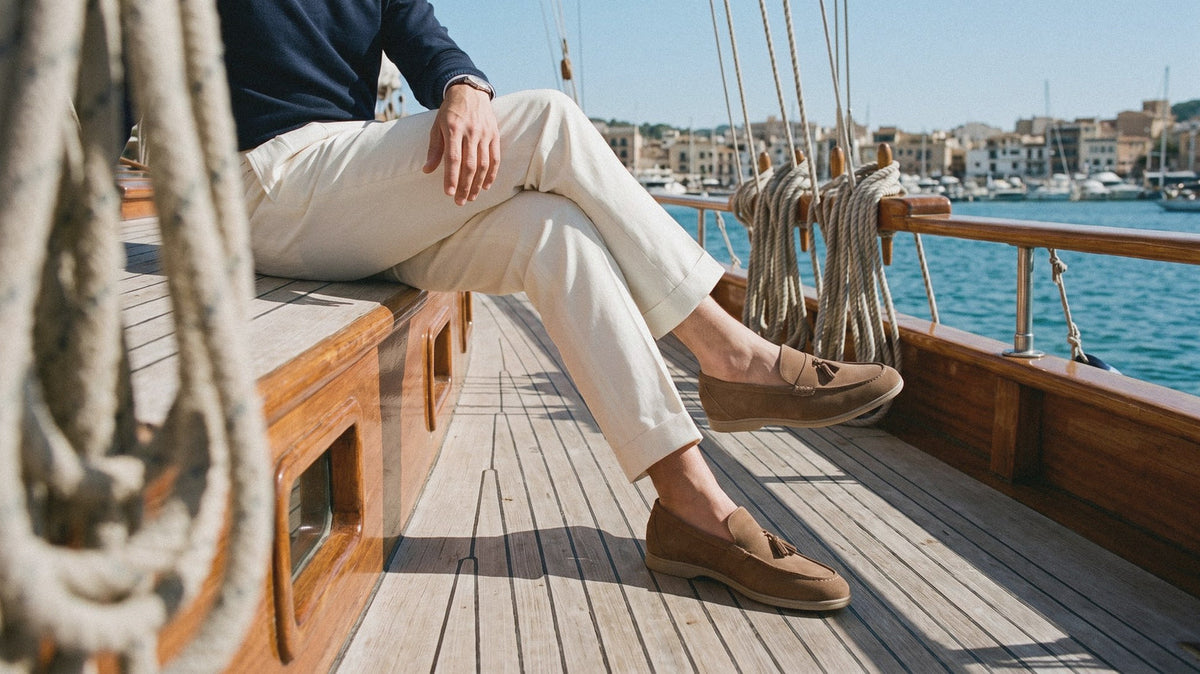 Brown suede-look penny loafers and cream pleated trousers on the teak deck of a yacht