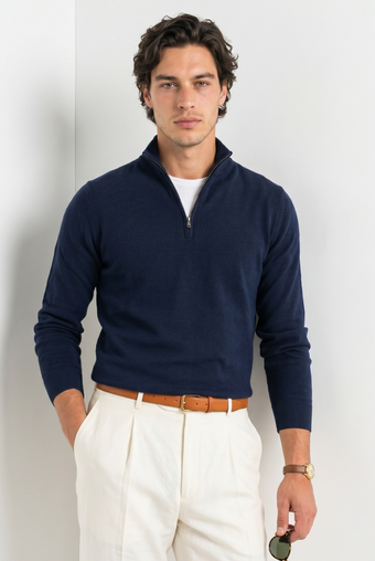Man wearing a navy quarter-zip sweater and white pants against a light background