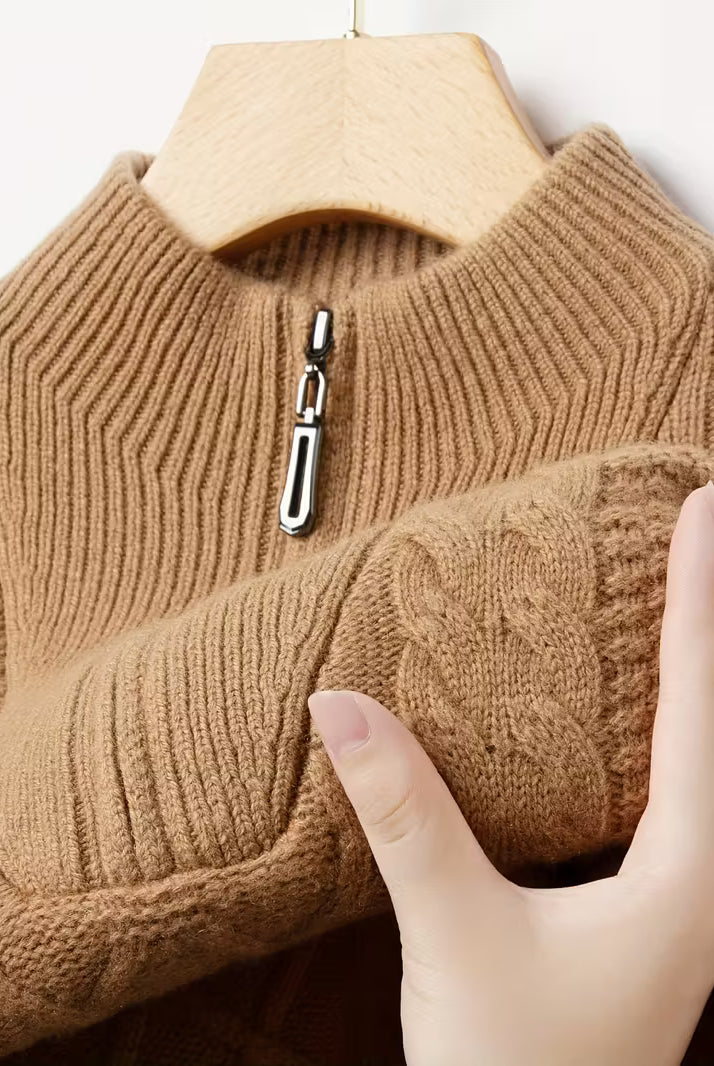 Brown knitted sweater with a zipper being held by a hand on a hanger.
