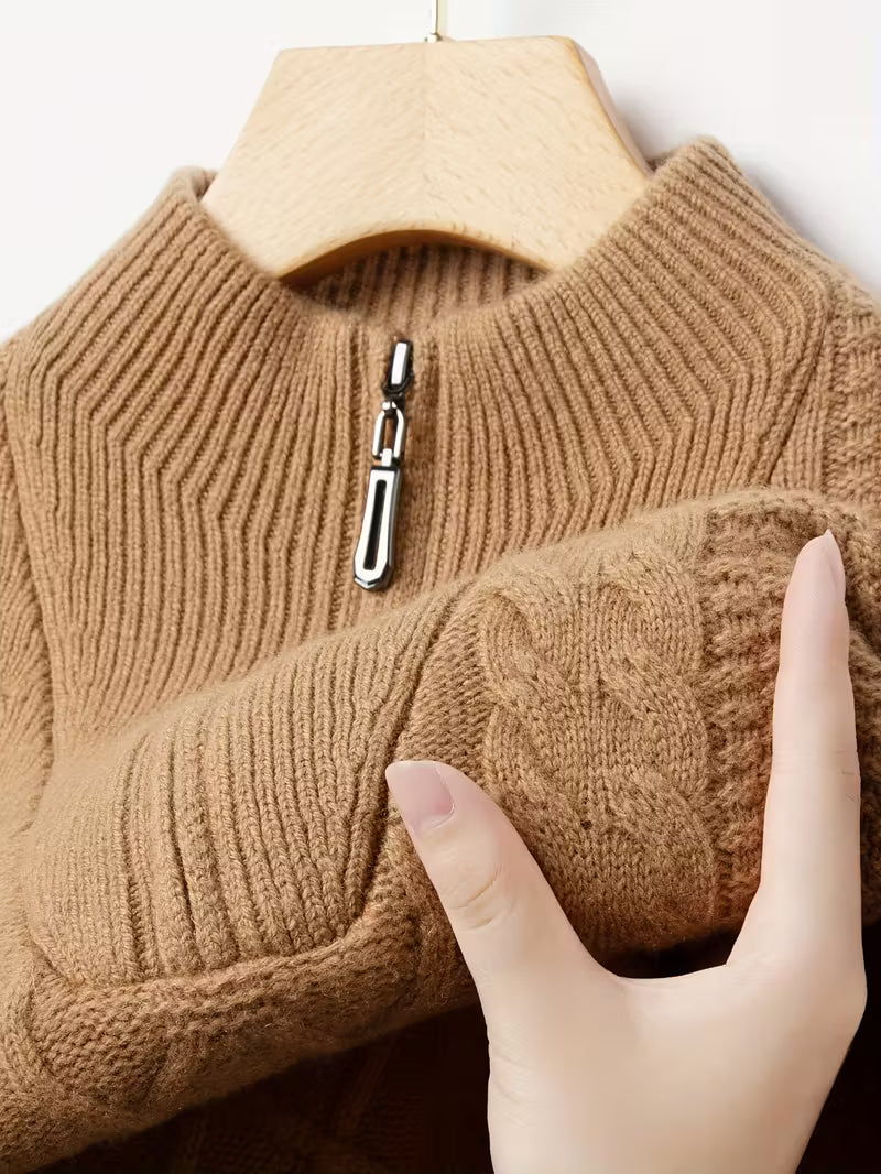 Brown knitted sweater with a zipper being held by a hand on a hanger.