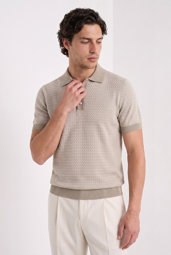 A man wearing a beige short-sleeve polo shirt with a subtle geometric pattern and cream trousers, standing against a plain white studio background.