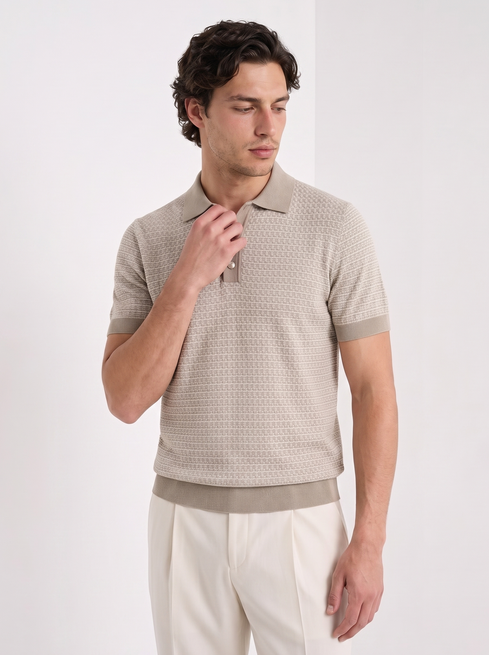 A man wearing a beige short-sleeve polo shirt with a subtle geometric pattern and cream trousers, standing against a plain white studio background.