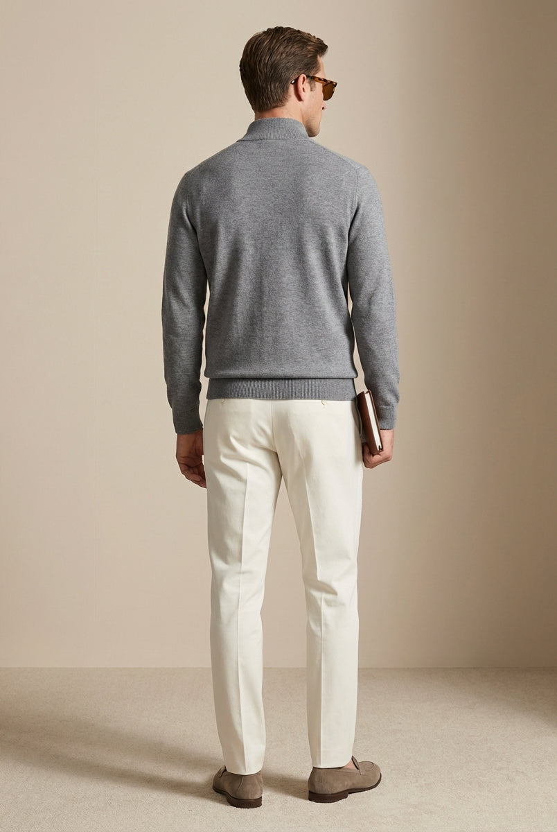 Man wearing a gray sweater and white pants against a beige background