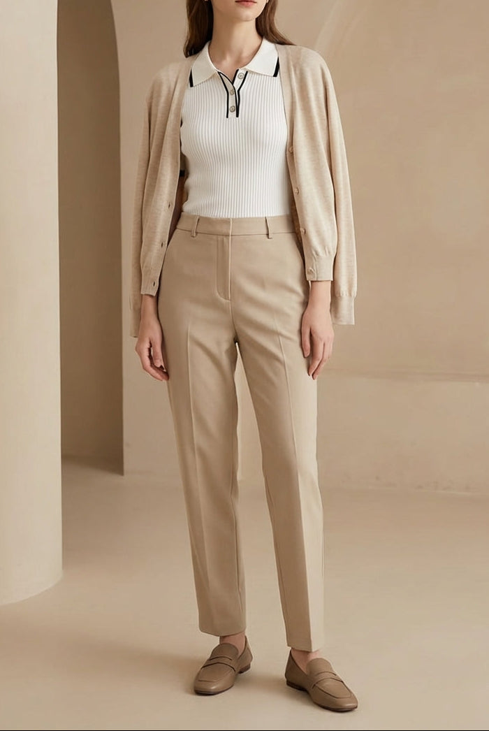 Woman wearing a beige cardigan, white shirt, and beige pants in a neutral setting