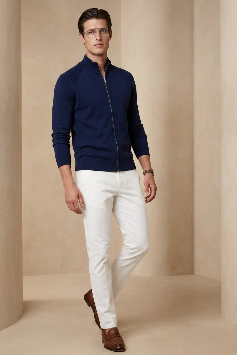 Man wearing a navy blue zip-up sweater, white pants, and brown shoes on a beige background