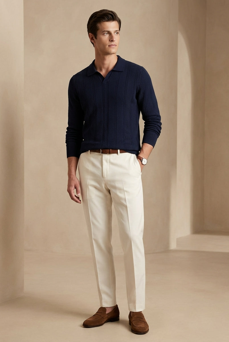Man wearing a navy sweater, white pants, and brown shoes against a beige background