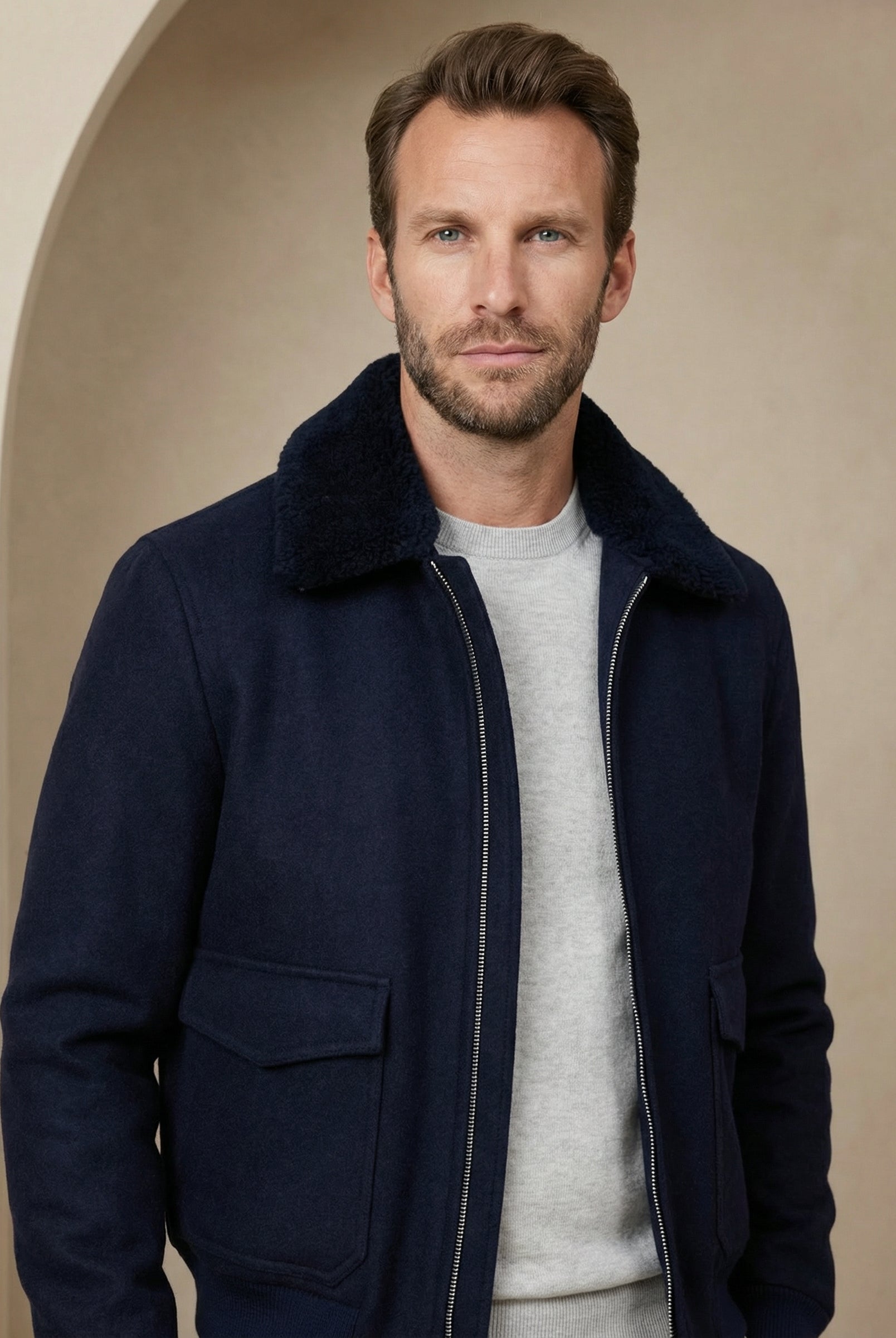 Man wearing a navy blue coat over a light gray sweater against a beige background