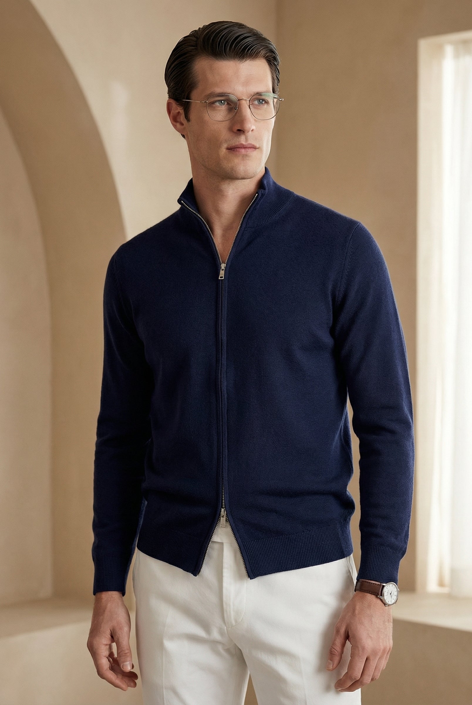 Man wearing a navy blue zip-up sweater and white pants in a bright room.