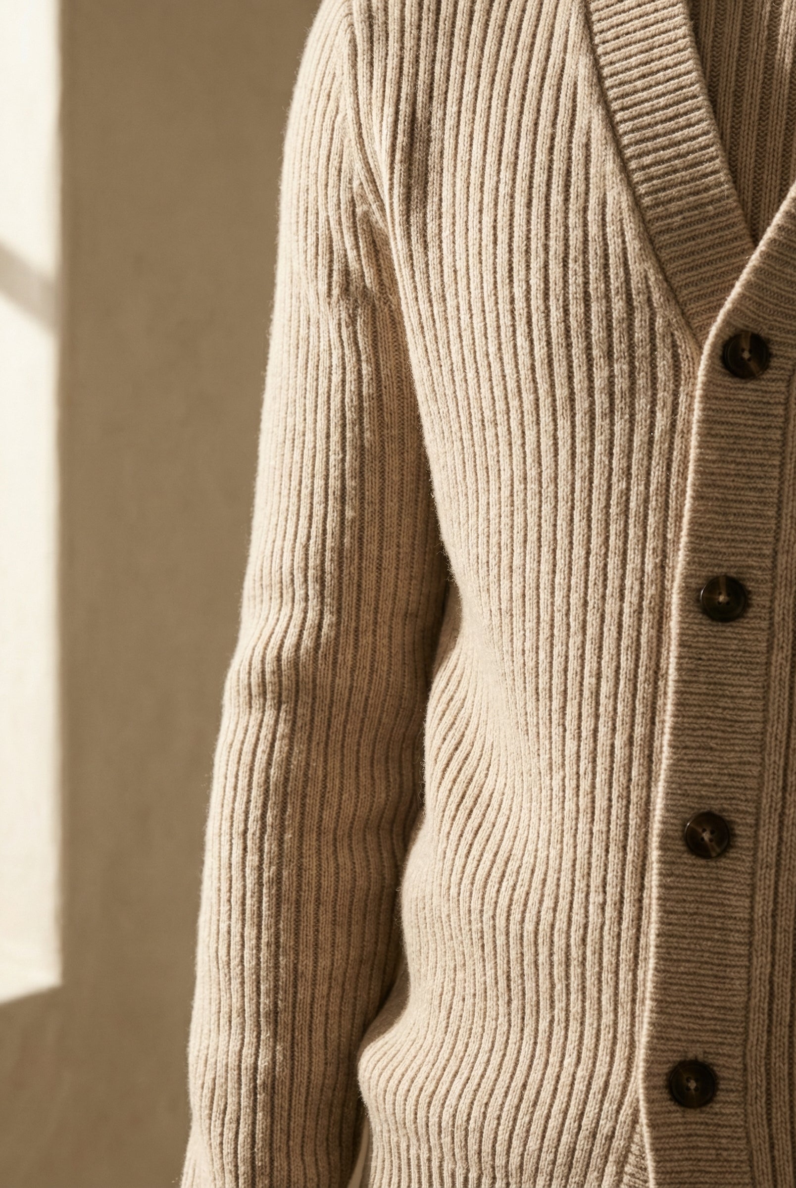 Close-up of a beige ribbed sweater with buttons against a neutral background