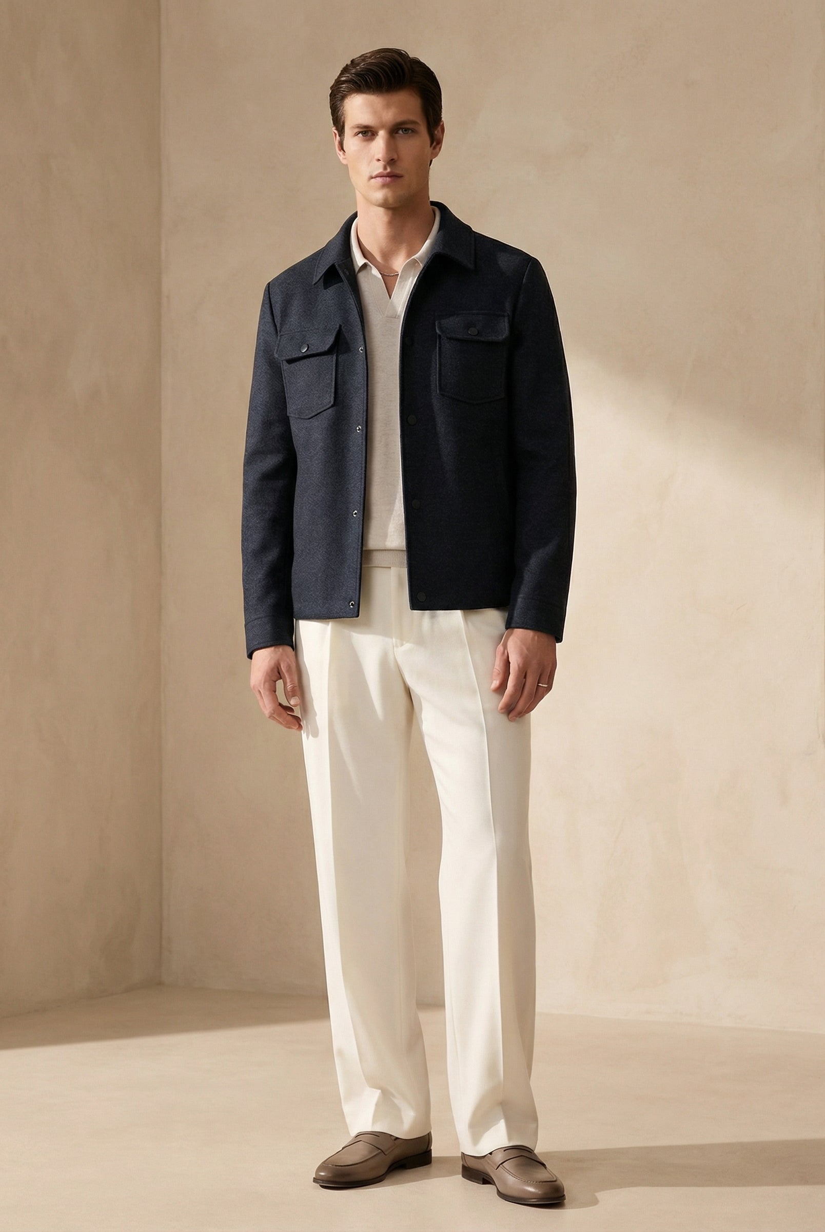 Man wearing a navy jacket over a white shirt with light-colored pants against a beige background
