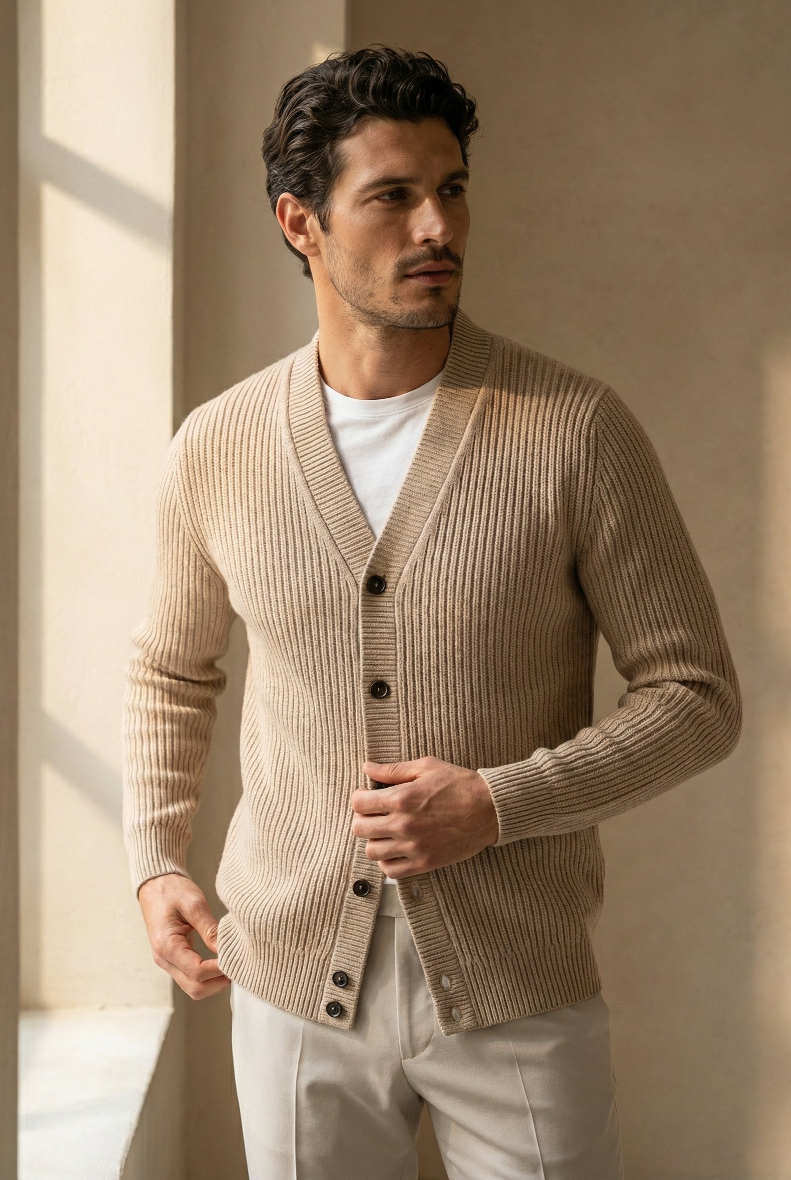 Man wearing a beige cardigan over a white shirt in a softly lit room.