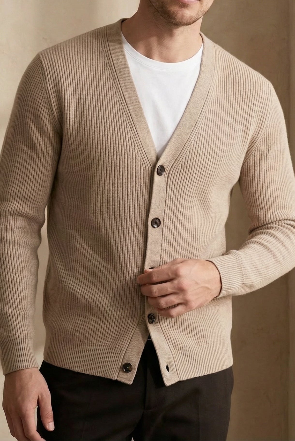 Man wearing a beige cardigan over a white shirt with a neutral background