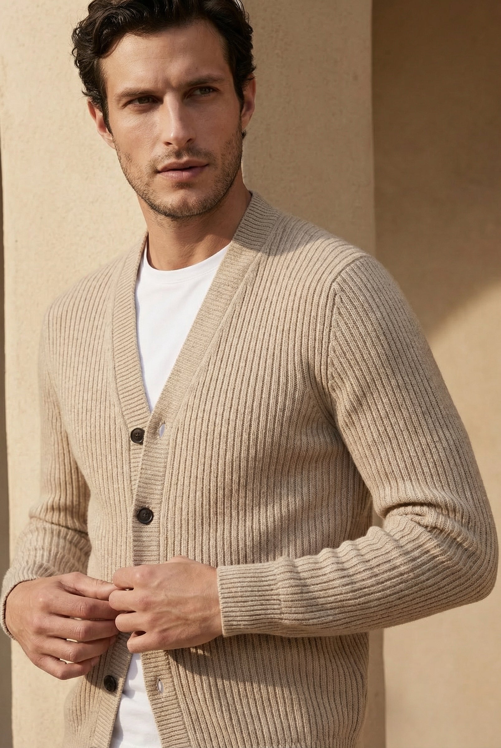 Man wearing a beige cardigan over a white shirt against a beige wall