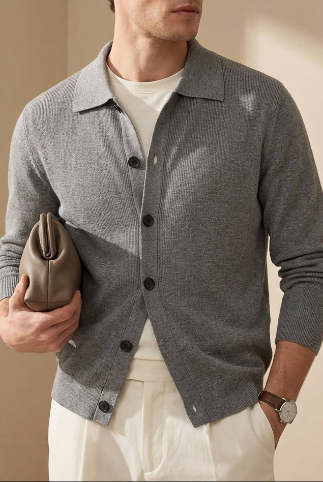Man wearing a gray cardigan over a white shirt, holding a brown leather clutch against a beige background.