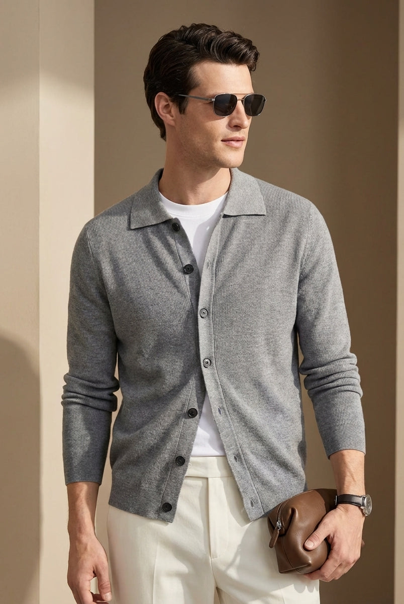 Man wearing a gray button-up shirt over a white t-shirt, sunglasses, and holding a brown leather jacket against a beige background.