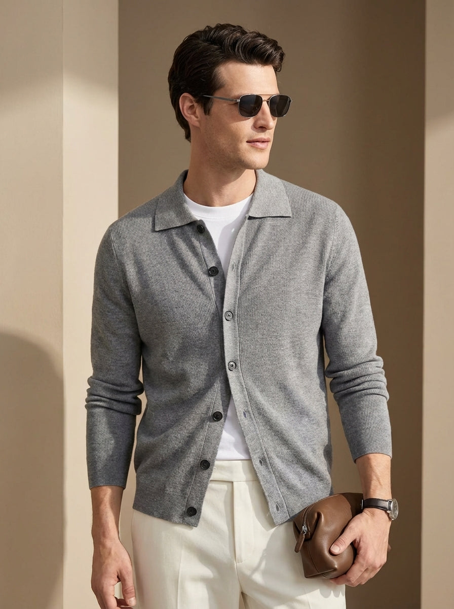 Man wearing a gray button-up shirt over a white t-shirt, sunglasses, and holding a brown leather jacket against a beige background.