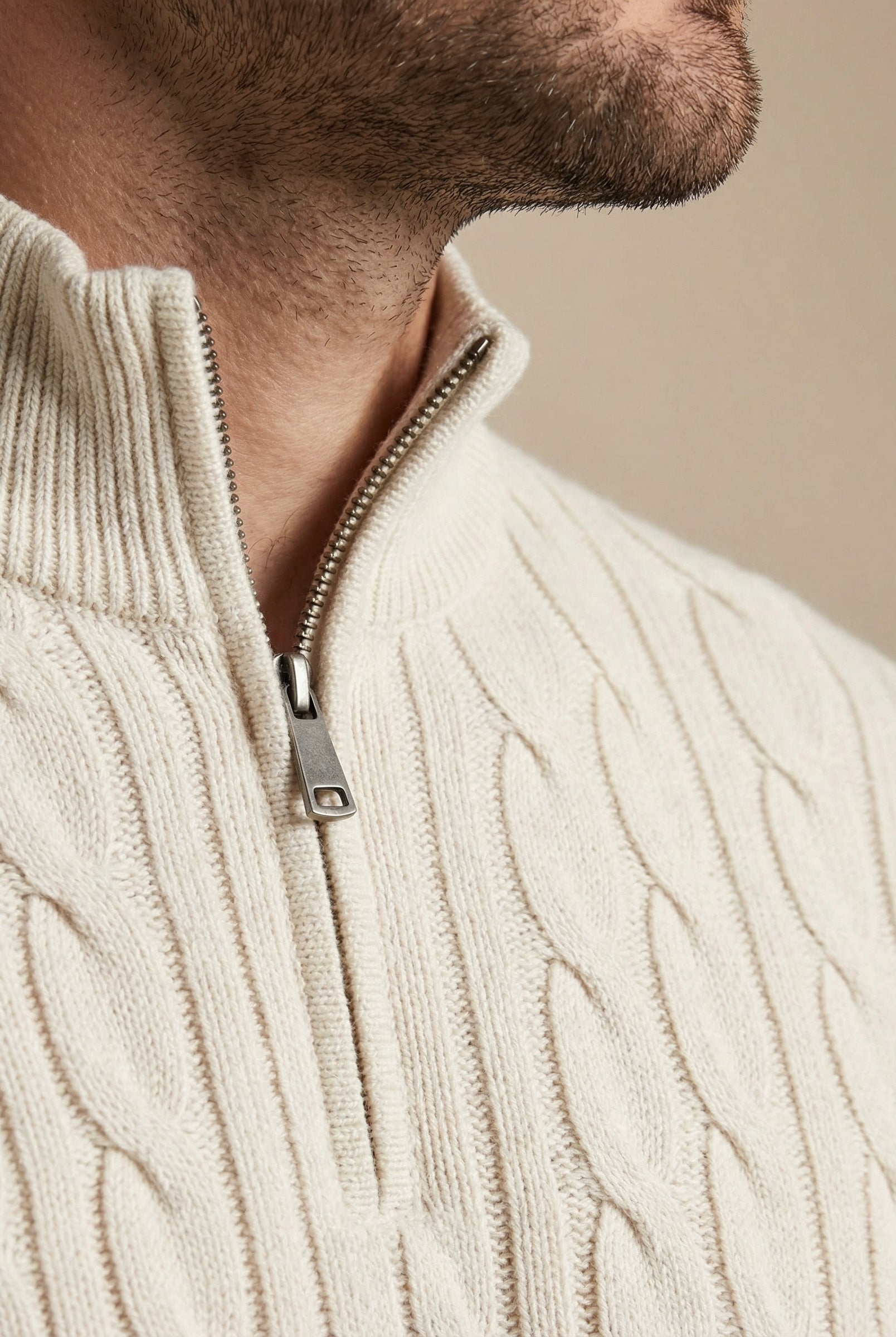 Close-up of a person wearing a cream cable knit sweater with a zipper.