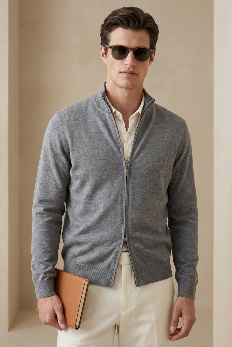 Man wearing a gray zip-up sweater over a white shirt, holding a brown leather folder against a beige background.