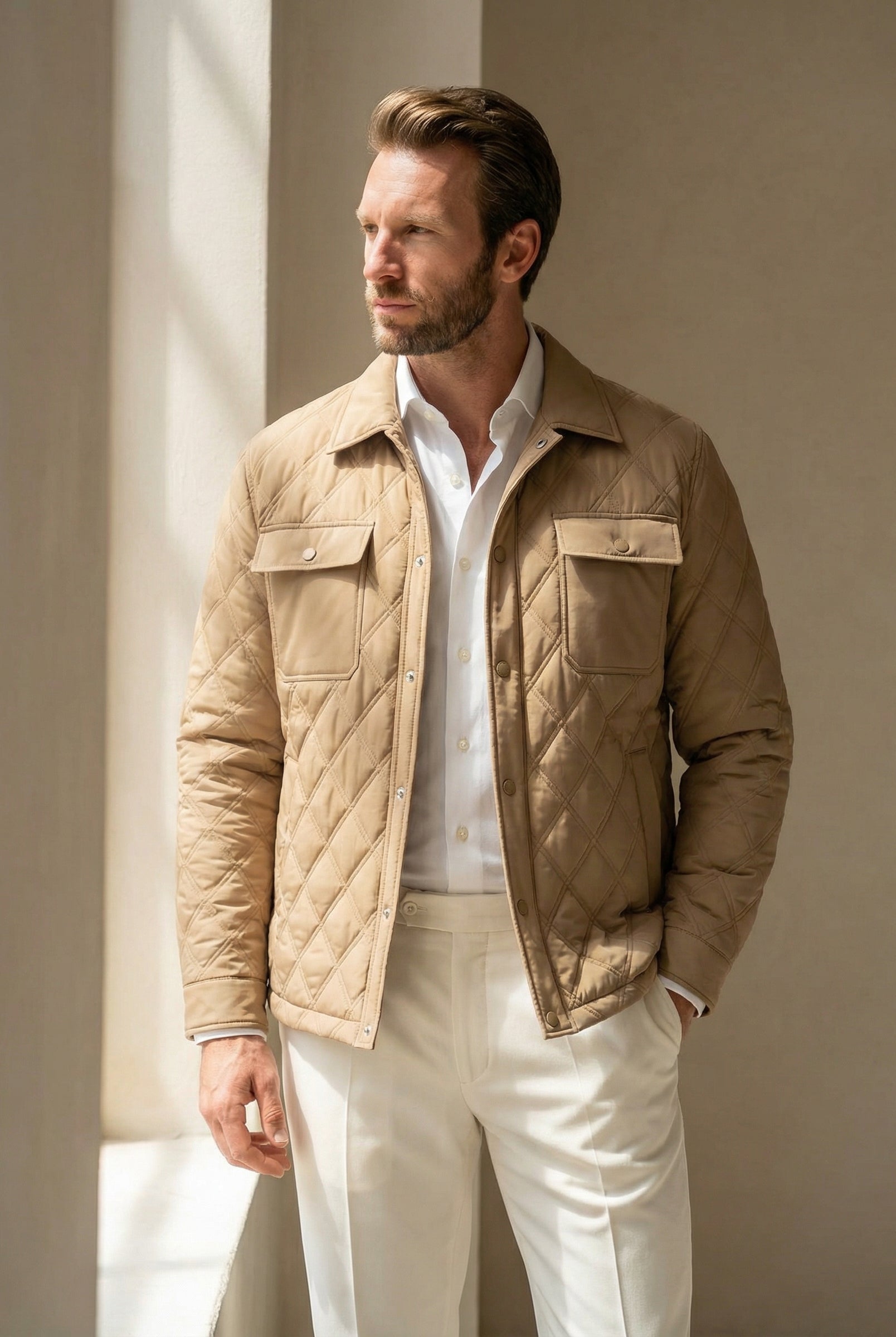 Man wearing a beige quilted jacket over a white shirt and pants, standing against a neutral background.
