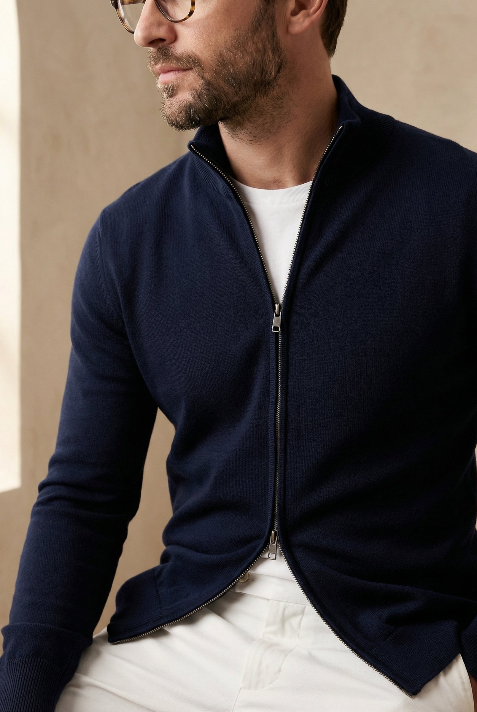 Man wearing a navy blue zip-up sweater over a white shirt against a beige background