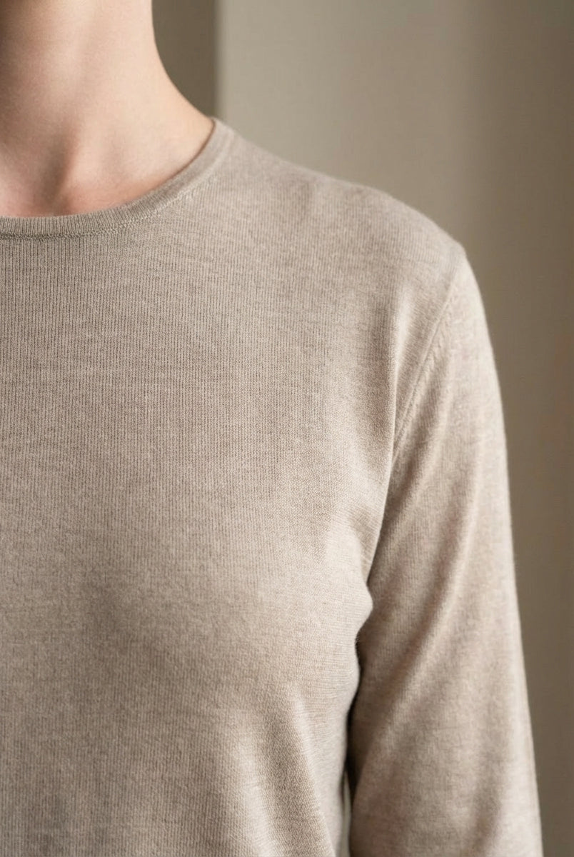 Close-up of a person wearing a beige long-sleeve shirt against a neutral background