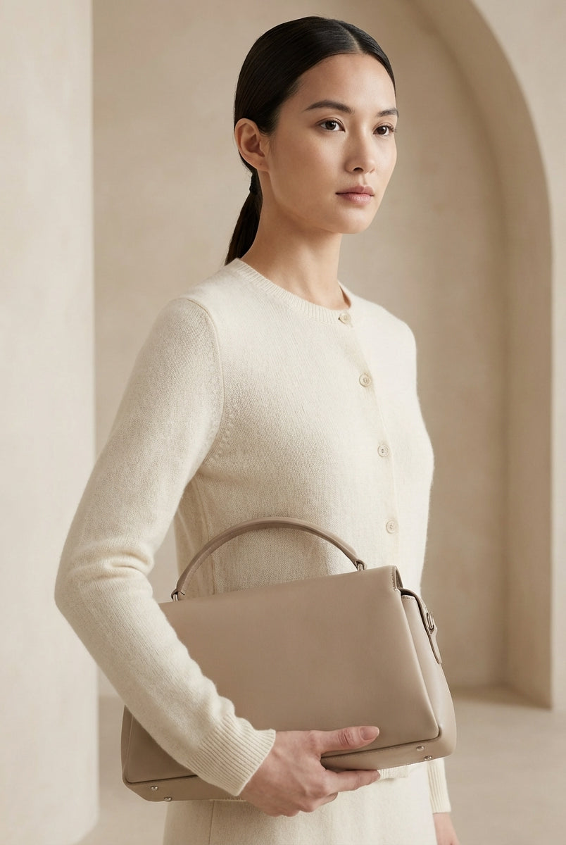 Woman holding a beige handbag against a neutral background