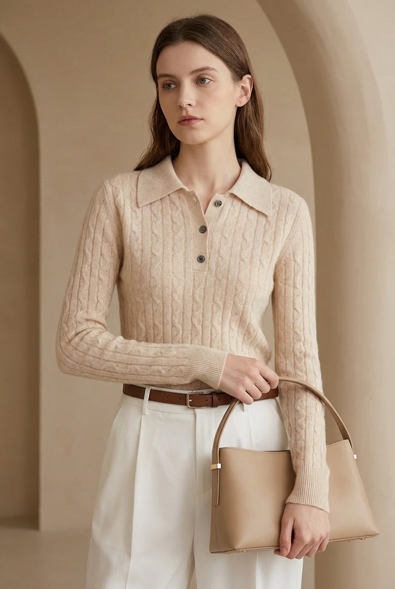 Woman wearing a beige cable knit sweater holding a matching handbag in an archway.
