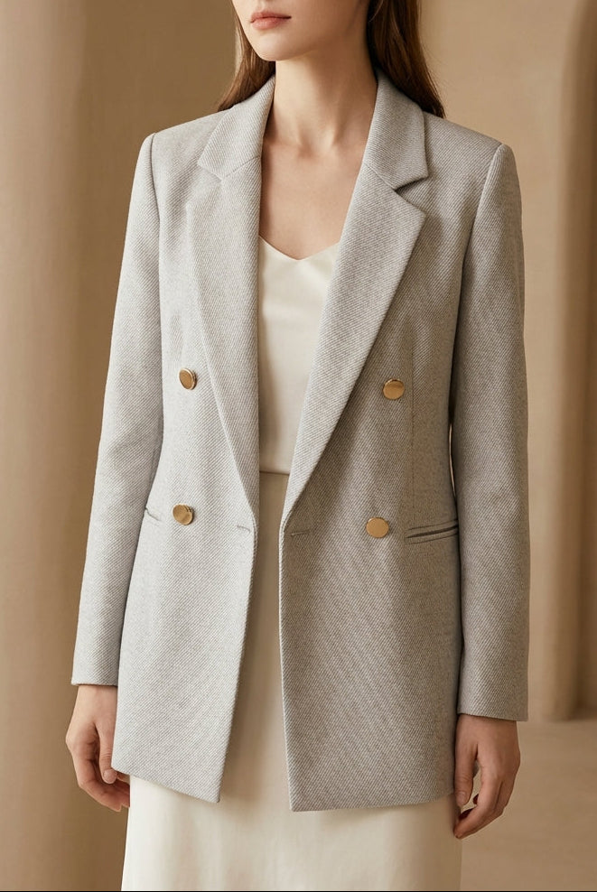 Woman wearing a gray blazer with gold buttons against a beige background, featuring the brand 'BLENIN'.
