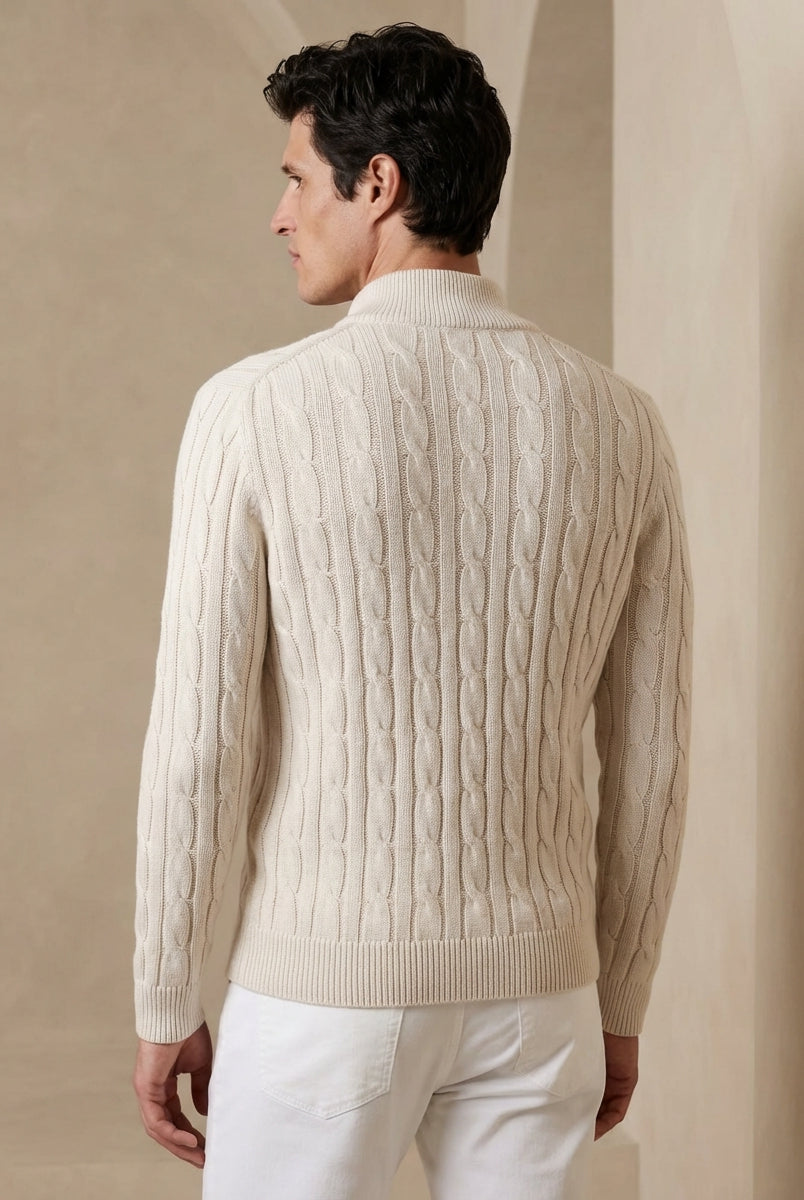 Man wearing a beige cable knit sweater against a beige wall