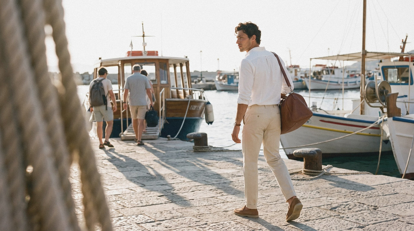Man carrying a brown leather weekend bag along a harbour quay