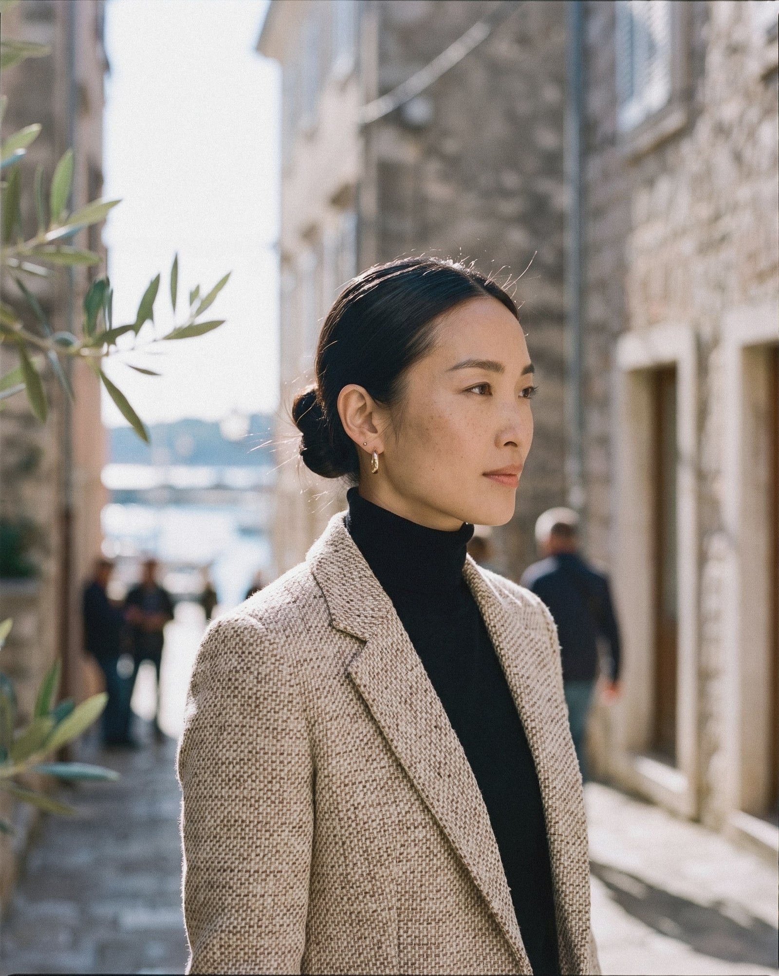 Woman with a sleek low bun in a tweed blazer walking through an old town