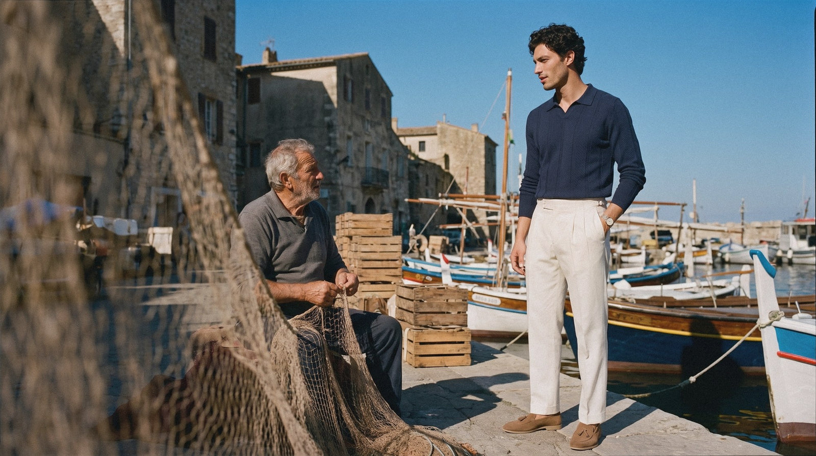 Man in a navy knitted polo, cream gurkha trousers and suede loafers on a harbour