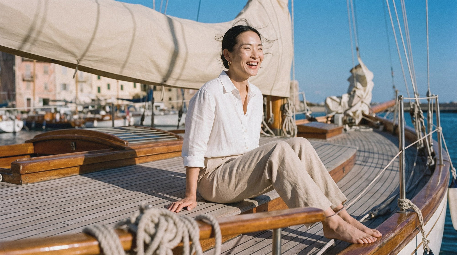 Woman in a white linen shirt and beige wide-leg trousers on the deck of a wooden sailing yacht