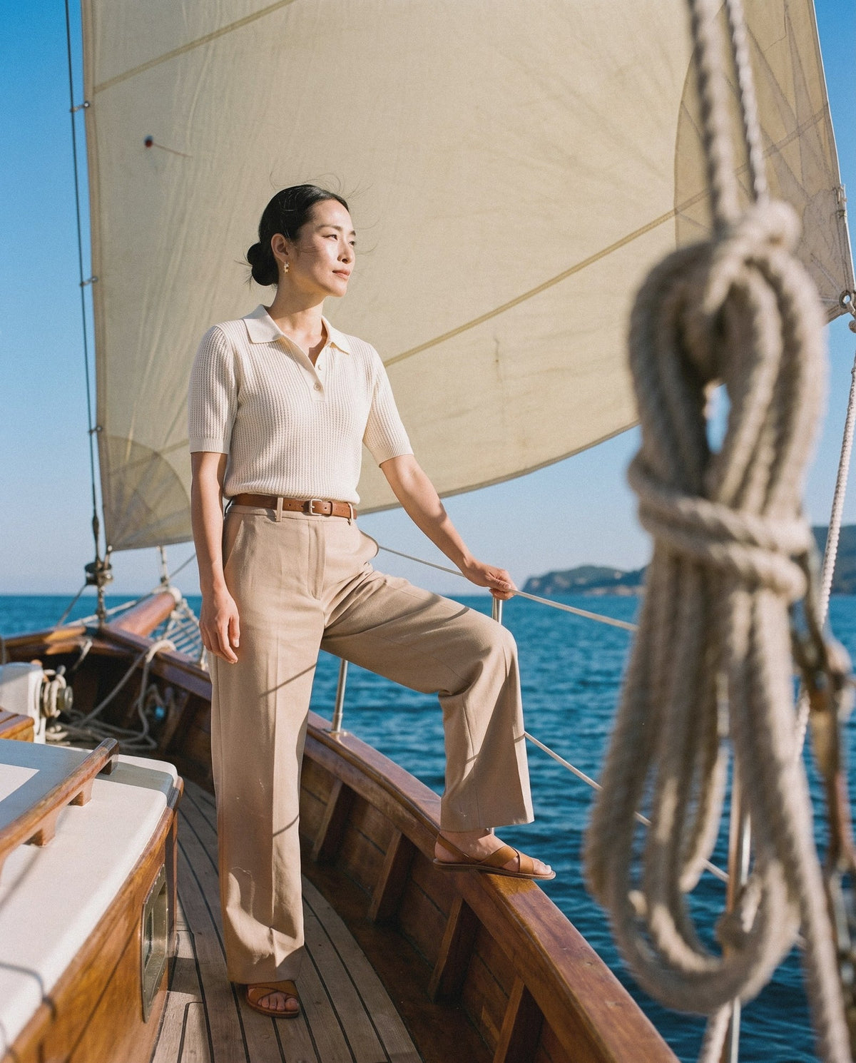Woman in a cream knitted polo and wide-leg trousers on a sailing boat