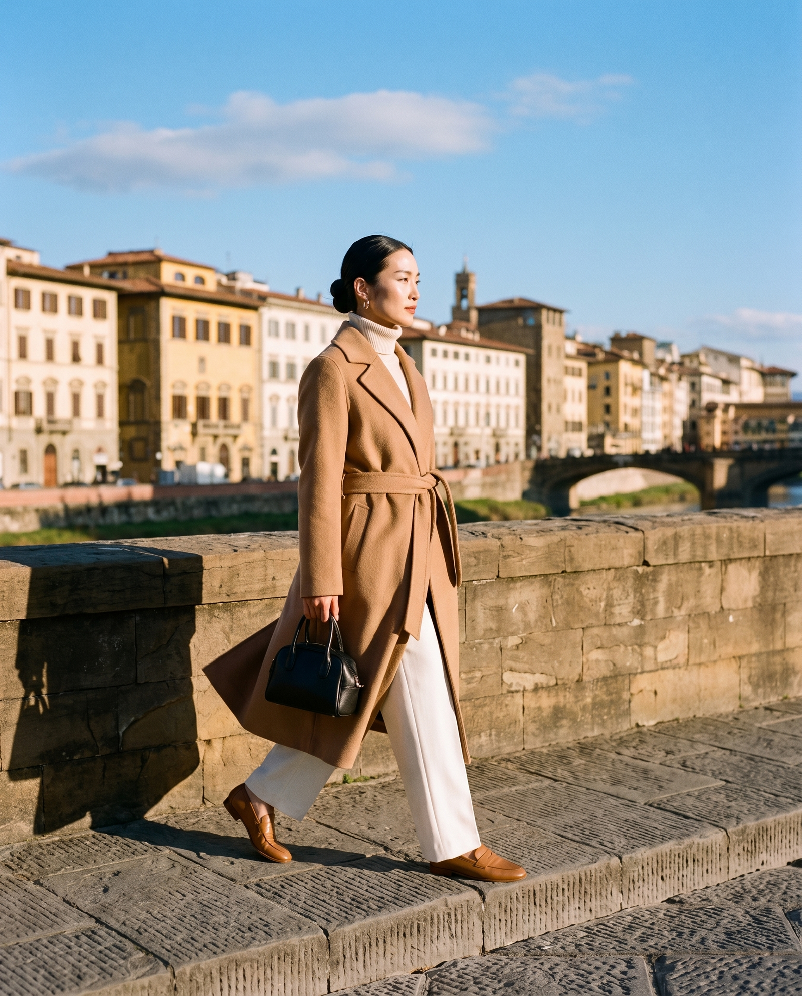 Woman in a long camel wrap coat on an old stone bridge in winter