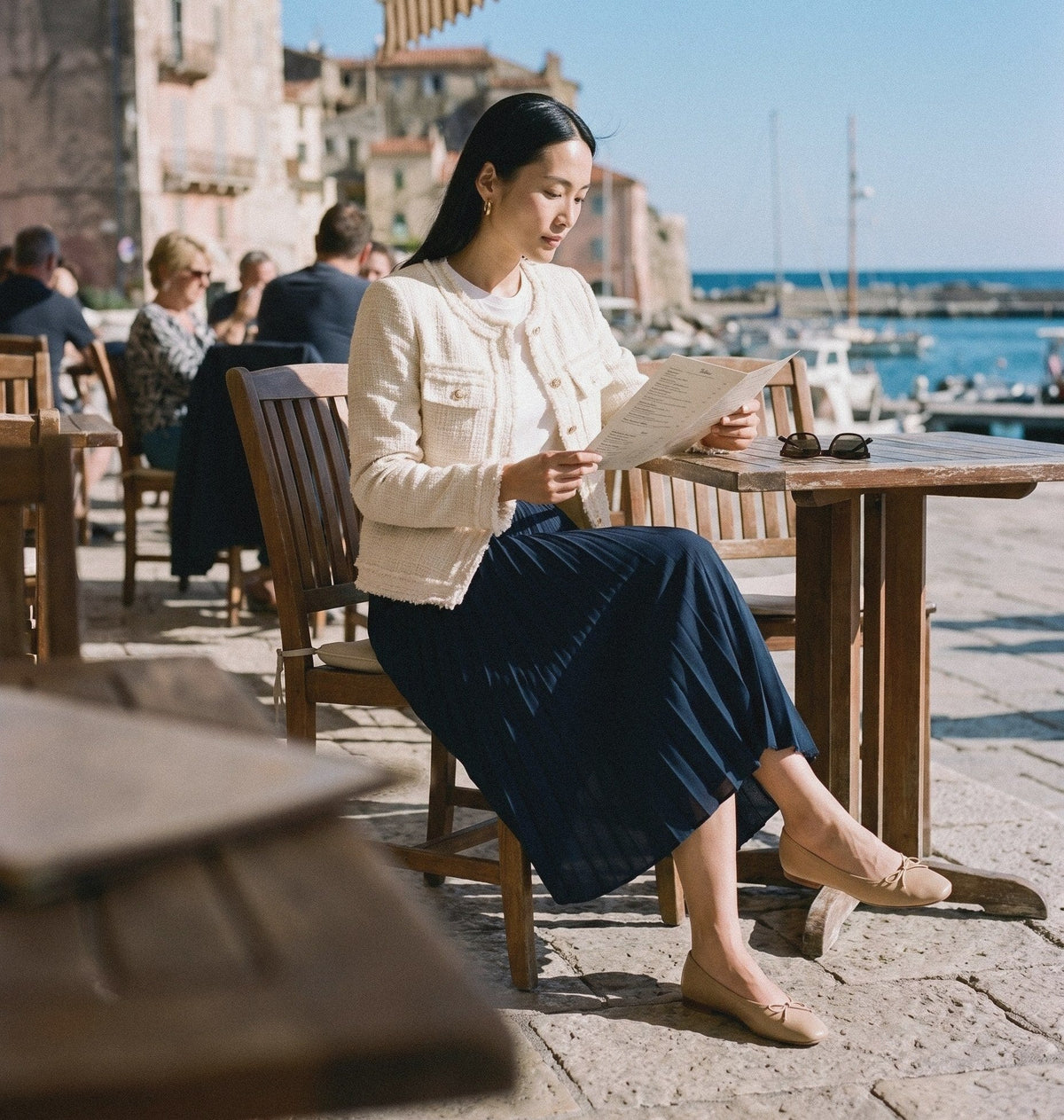 Woman in a cream tweed blazer and navy pleated skirt at a harbour café – BLENIN women's bestsellers