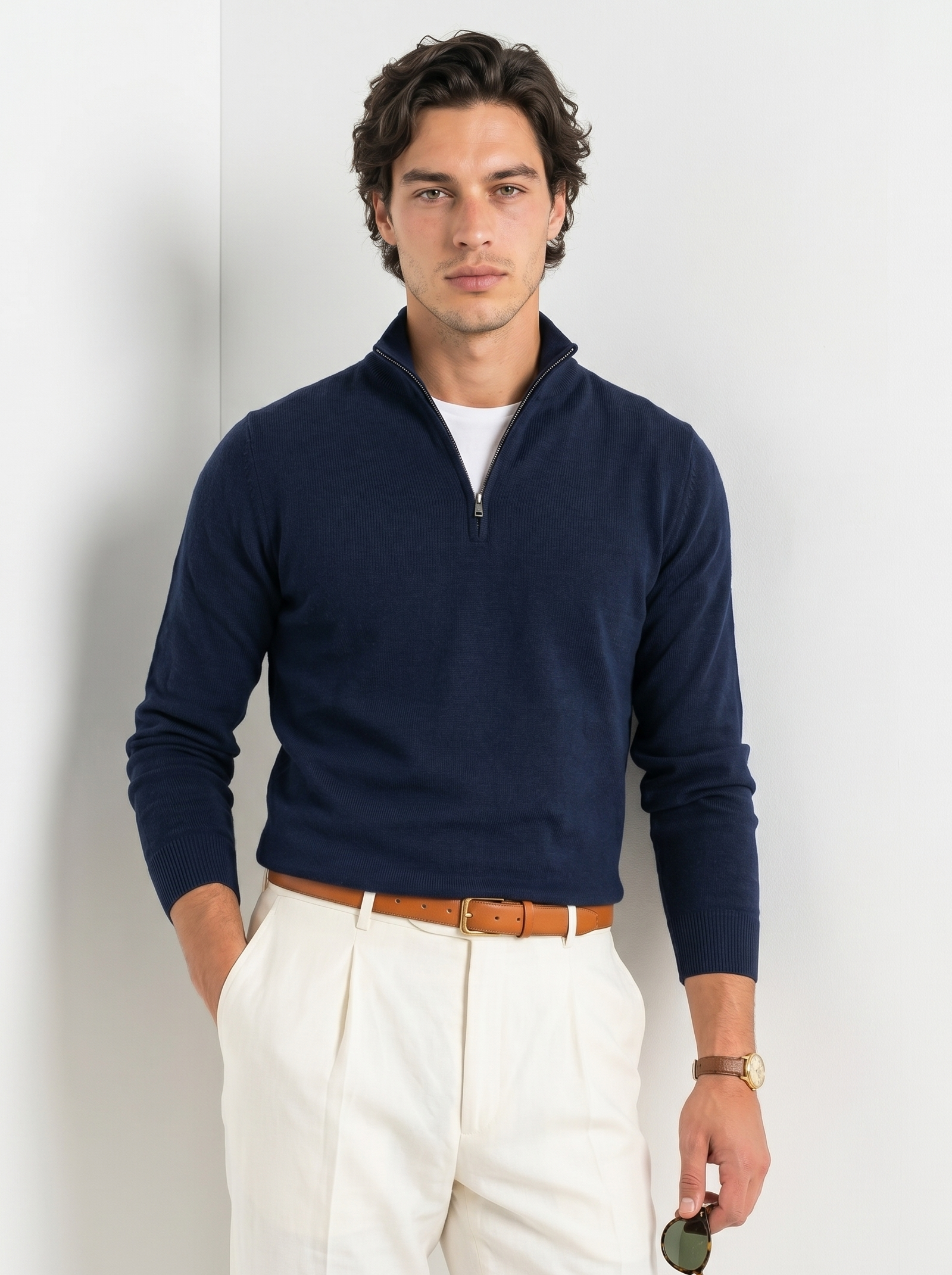 Man wearing a navy quarter-zip sweater and white pants against a light background