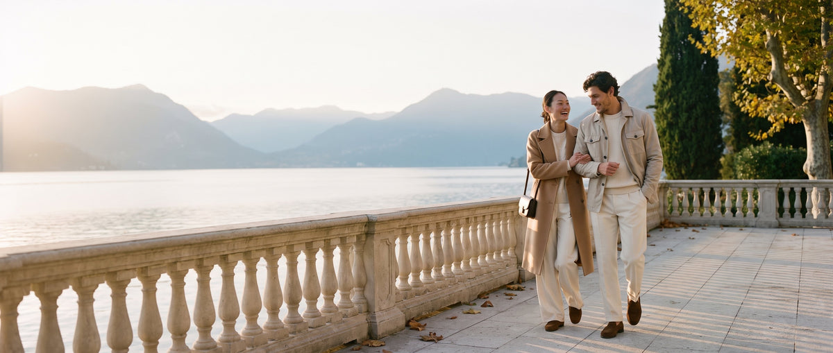 Couple in BLENIN autumn coats and cream trousers walking on a lakeside villa terrace