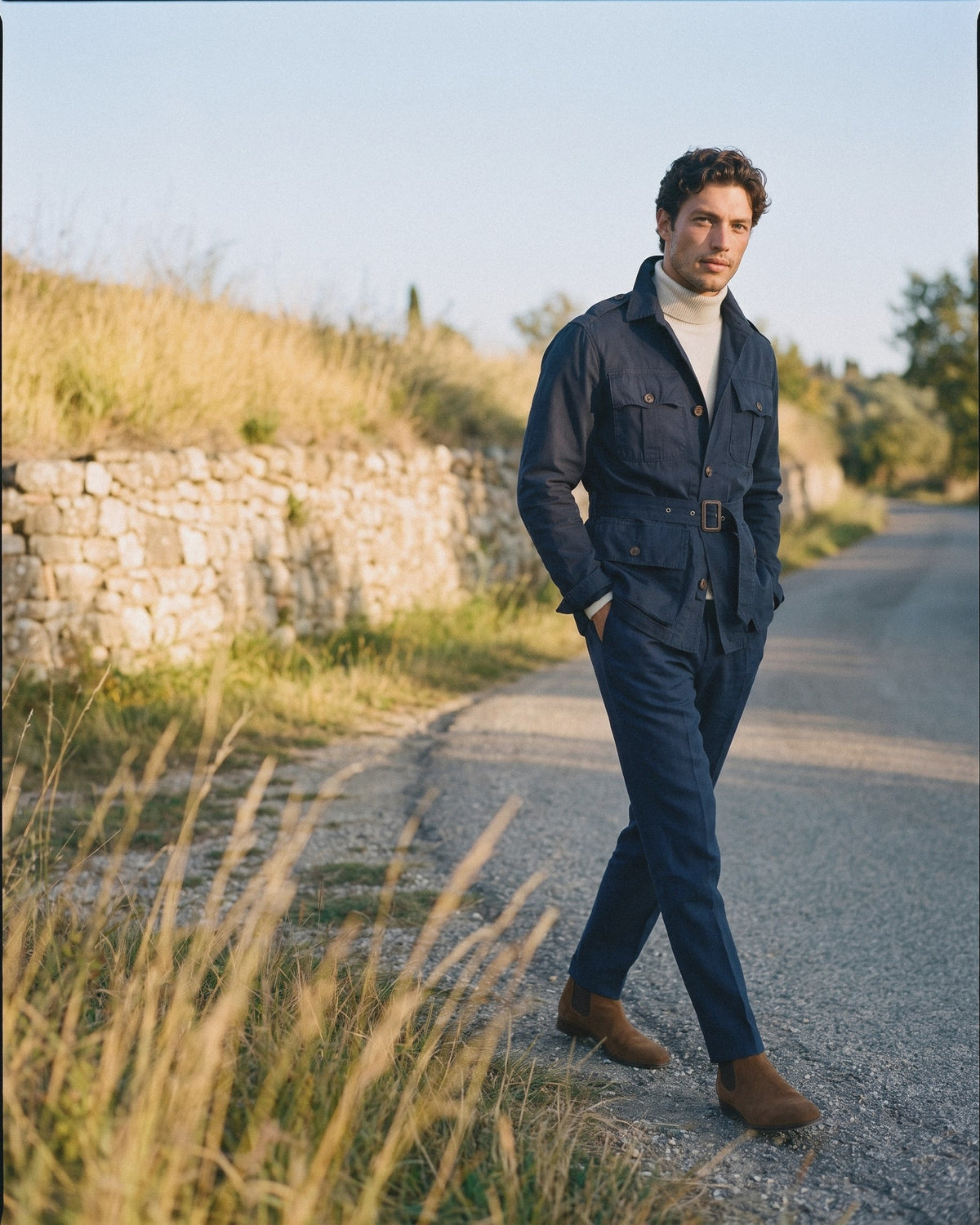 Man in a navy belted field jacket and navy pleated trousers on an autumn day