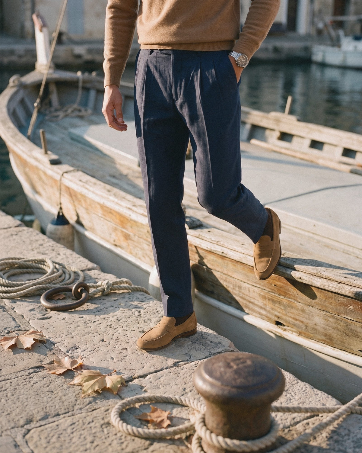 Man in navy pleated trousers and tan suede loafers stepping off a wooden boat