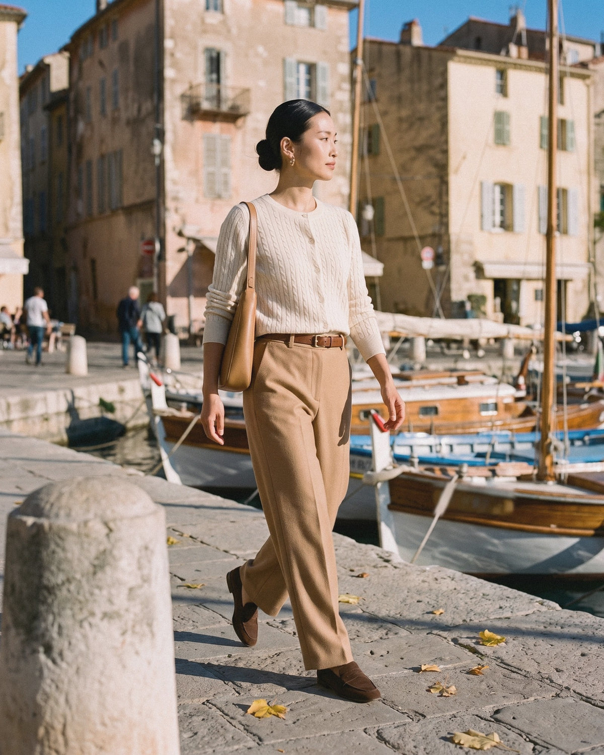 Woman in an ivory cable-knit top and camel wide-leg trousers walking along a harbour
