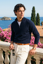 Man in navy sweater and white pants standing on a balcony with ocean view