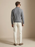 Man wearing a gray sweater and white pants against a beige background