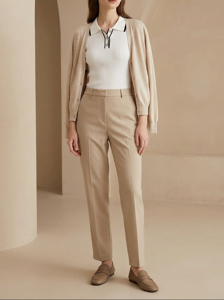 Woman wearing a beige cardigan, white shirt, and beige pants in a neutral setting