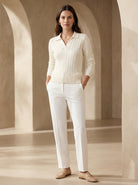 Woman wearing a white cable knit sweater and white pants in a beige archway setting