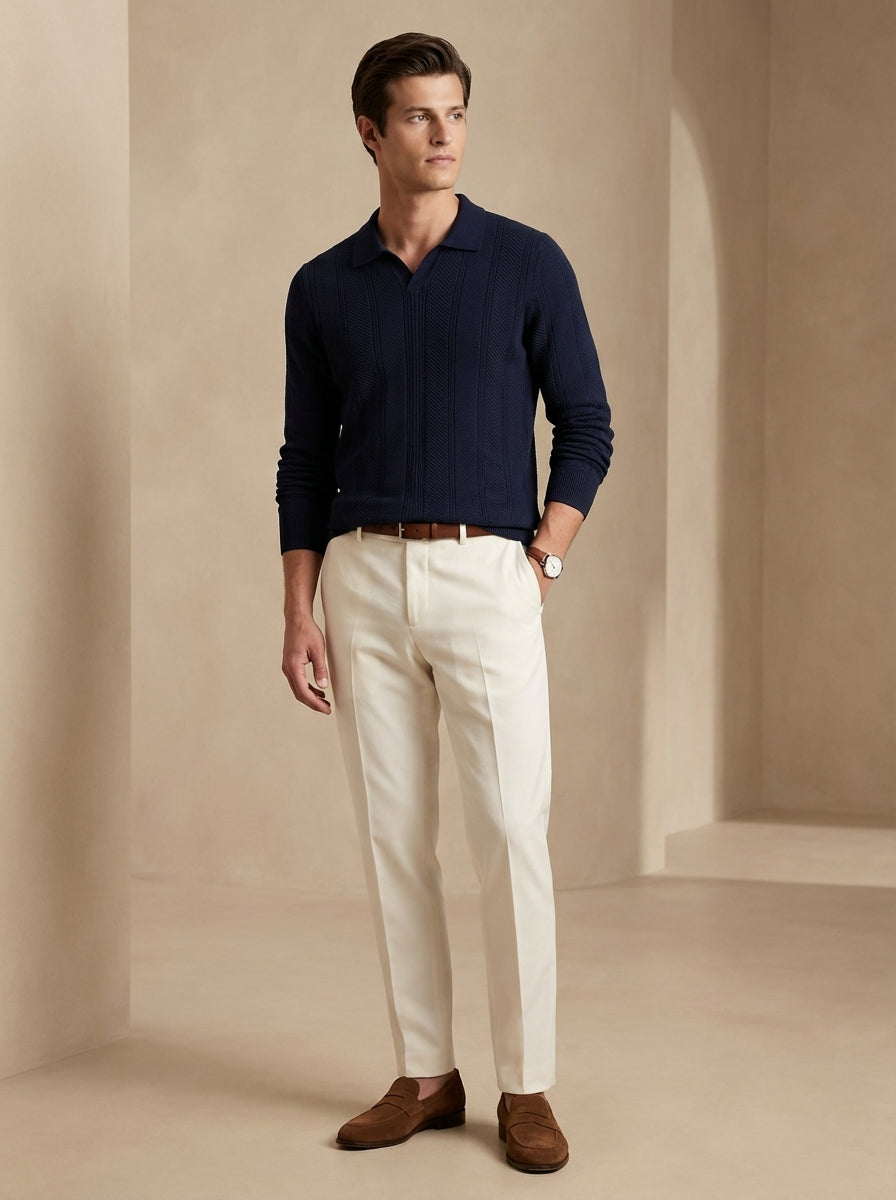 Man wearing a navy sweater, white pants, and brown shoes against a beige background