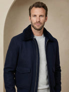 Man wearing a navy blue coat over a light gray sweater against a beige background