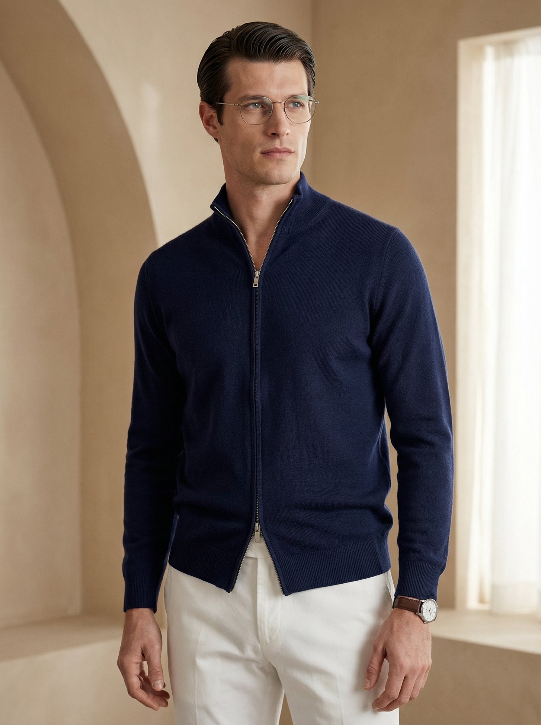 Man wearing a navy blue zip-up sweater and white pants in a bright room.