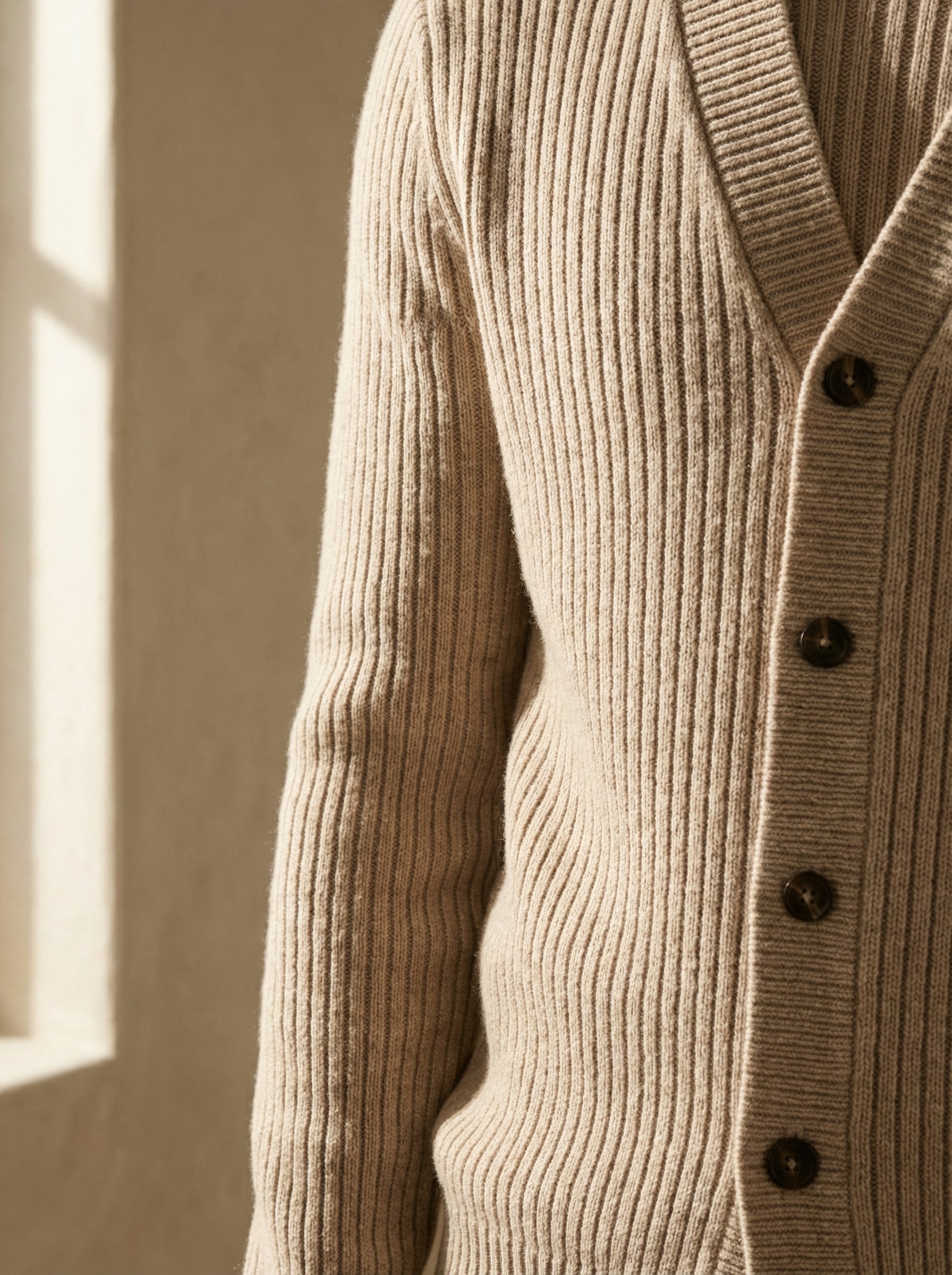 Close-up of a beige ribbed sweater with buttons against a neutral background